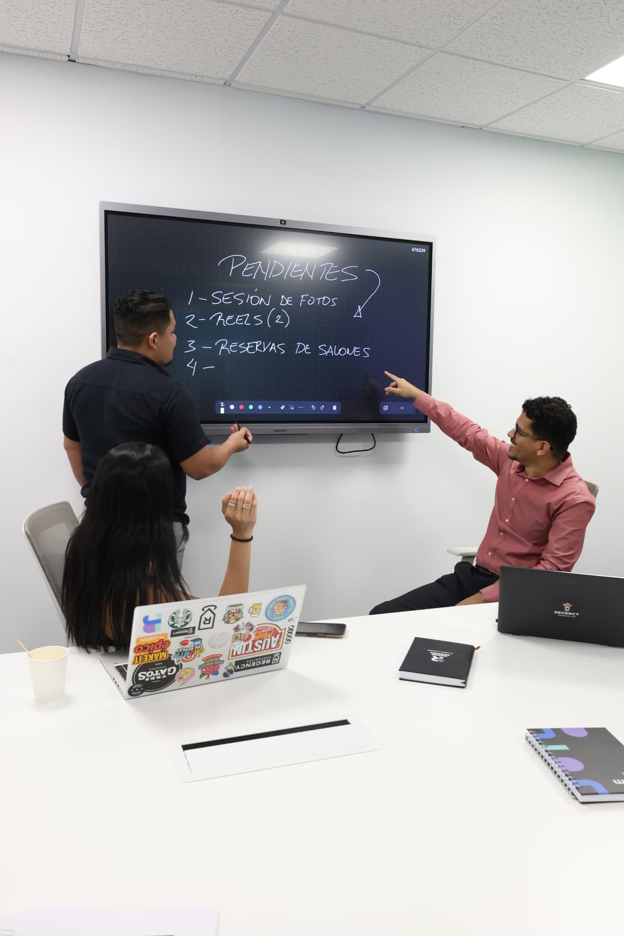 Sala de reuniones de Rworks con pantalla interactiva y equipo reunido alrededor de la mesa